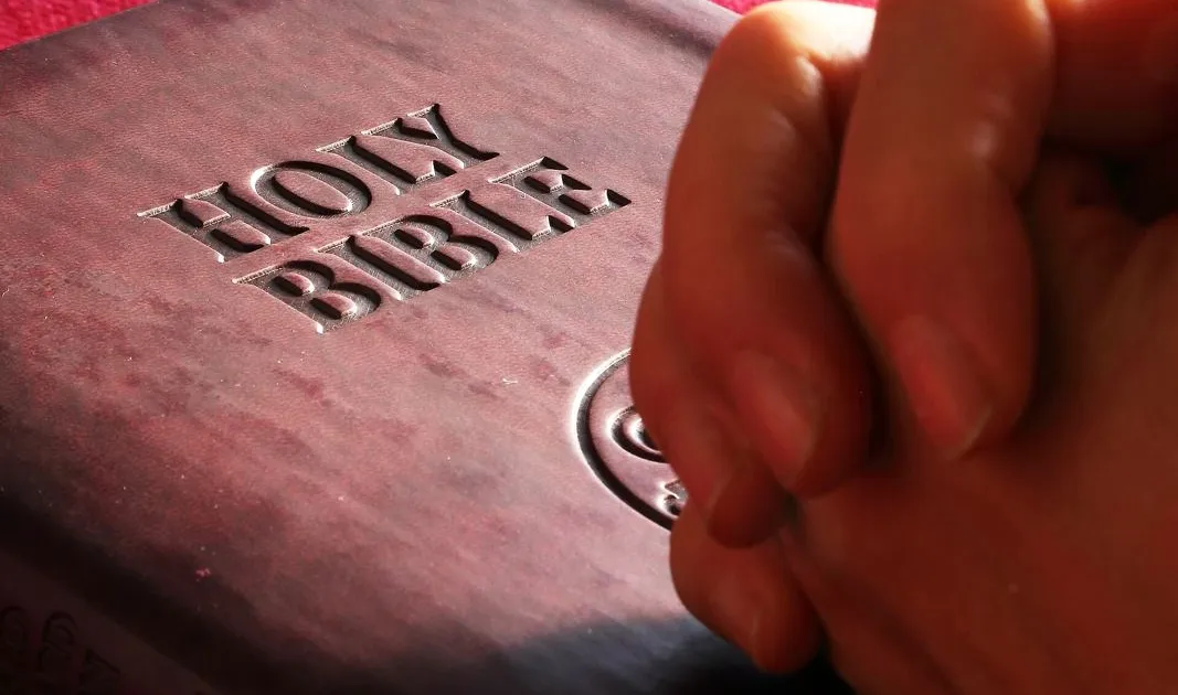 Manos que reposan sobre una Biblia en actitud de oración