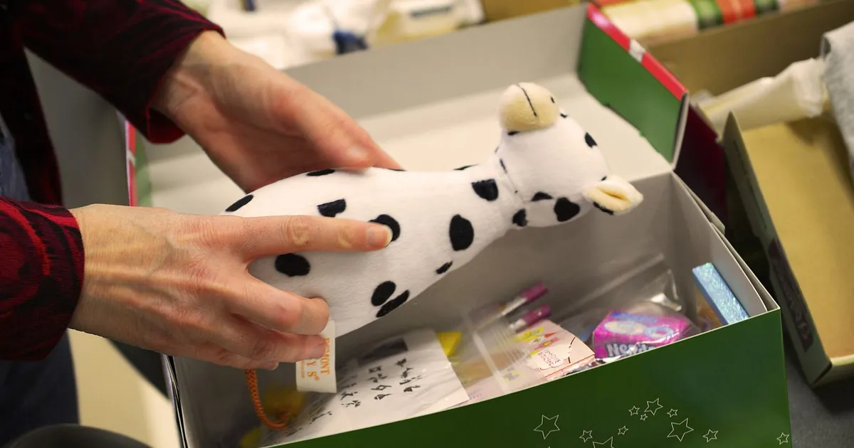 Manos de una voluntaria llenando una caja de zapatos de Operation Christmas Child con un peluche y material escolar (base aérea de Yokota, Japón, noviembre de 2016)